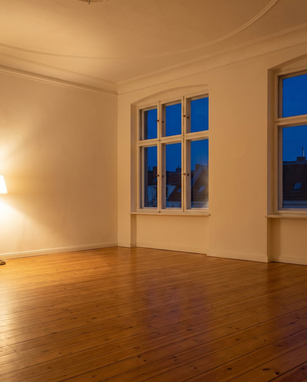 Leerer Altbau-Wohnraum mit hohen Fenstern und Dielenboden